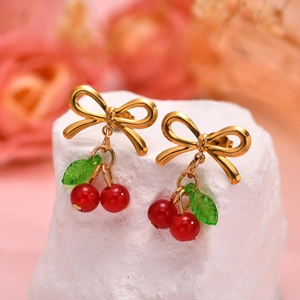 Boucles d'oreilles nœud doré avec perles cerises rouges et feuille verte sur pierre
