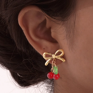 Gros plan de boucles d'oreilles nœud doré avec cerises rouges et feuilles vertes