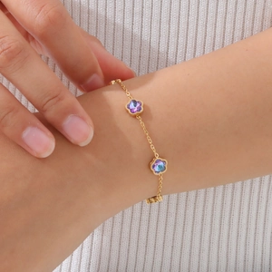 Nahaufnahme eines goldenen Armbands mit violetten Kristallblütenanhängern am Handgelenk