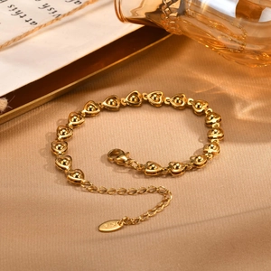 Macro detail of golden stainless steel heart chain bracelet with round bead accents