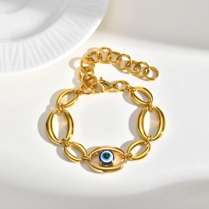 Gold stainless steel oval link bracelet with blue evil eye charm on white ceramic