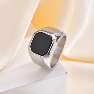 Gros plan d'une bague chevalière pour homme en acier avec agate noire sur marbre et soie