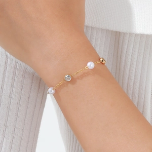 Dettaglio del bracciale dorato in acciaio con perle bianche e zircone scintillante
