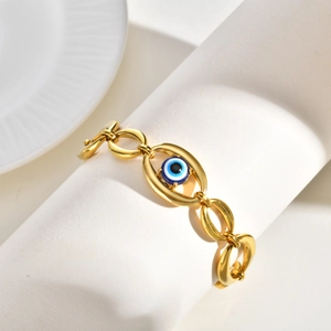 Detailed view of gold plated evil eye bracelet wrapped on a minimalist white cylinder stand