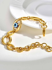 Detail shot of a chunky gold oval link bracelet featuring a classic blue evil eye charm