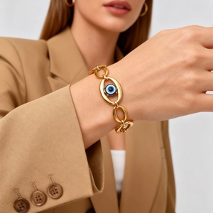Close-up of a gold thick chain bracelet with a blue evil eye charm on a model wrist