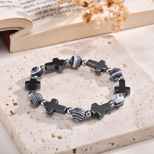 Close-up of a beaded cross bracelet with black stone and striped marble beads on stone base
