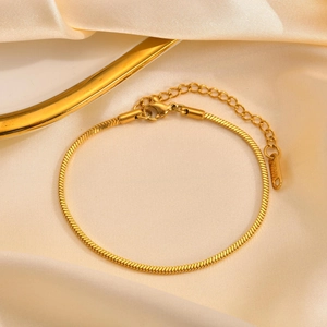 Detail of gold square snake chain bracelet with lobster clasp on silk fabric