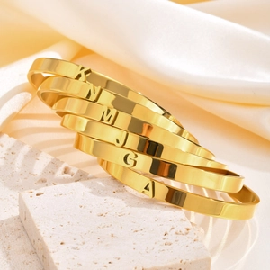 Détail macro de bracelets lettres en acier doré poli sur support en pierre