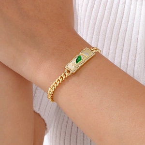 Macro shot of gold Cuban link bracelet with a green gemstone pendant and crystal border