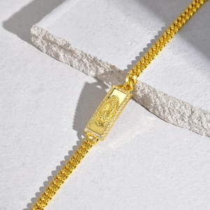 Macro view of gold Cuban link bracelet featuring an iced-out Virgin Mary pendant and stones
