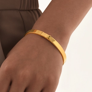 Détail d'un bracelet jonc doré poli avec une lettre A en relief sur une peau de mannequin