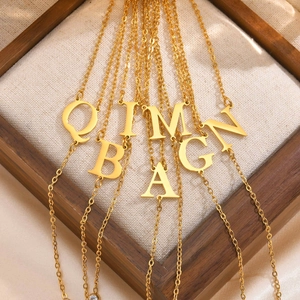 Close-up of gold-plated stainless steel initial pendants on a delicate cross chain