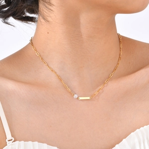 Close-up of golden paperclip chain necklace with a round zircon and a rectangular bar pendant