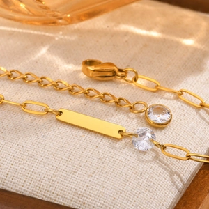 Macro detail of a gold titanium necklace featuring a polished bar and sparkling zircon stones