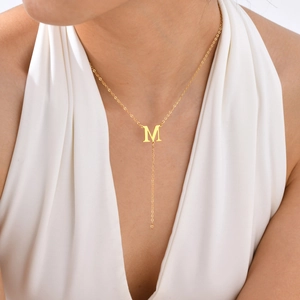 Detail of golden Y-shaped necklace with letter M pendant worn by a model on white background