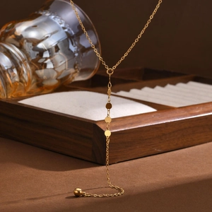 Dettaglio macro della collana a Y dorata con piccole paillettes tonde e pendente a sfera lucida