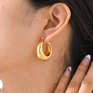 Close-up of golden ribbed C-shaped hoop earrings worn by a model in a lifestyle setting