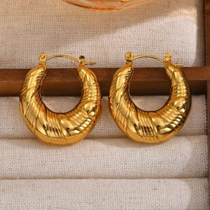 Detailed macro of gold C-shaped croissant hoop earrings with ribbed texture on cream fabric
