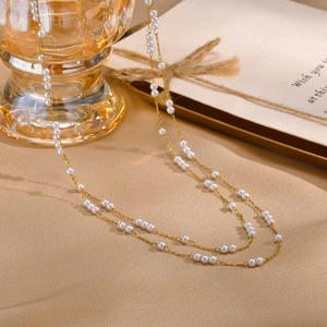 Élégant collier double épaisseur doré avec perles blanches sur fond chaud