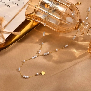 Macro detail of gold Y-shaped stainless steel necklace with white pearls and heart pendant