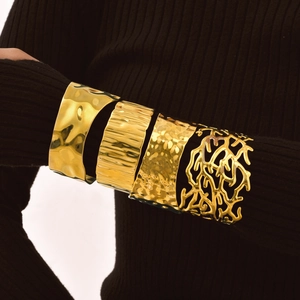 Detail of four-piece gold cuff bracelets with wavy, textured, and coral cut-out patterns