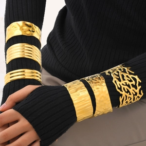 Close-up of golden wide irregular metal cuffs worn over black ribbed knit sleeves