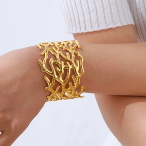 Close-up of a wide gold coral-inspired hollow cuff bracelet on a female model's wrist
