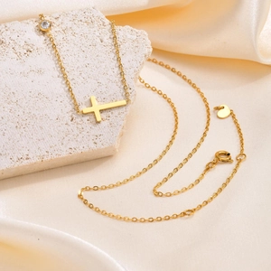 Goldene Edelstahlkette mit horizontalem Kreuz und weißem Zirkon auf hellem Stein