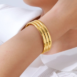 Polished gold triple-layered wide cuff bracelet on wrist with elegant minimalist style