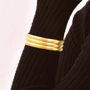 Close-up of golden irregular geometric wide cuff bracelet worn over a black sweater sleeve