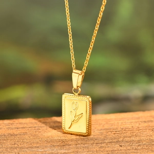 Gold stainless steel necklace with embossed tulip flower pendant on a rustic wood surface