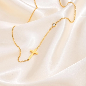 Goldene Halskette aus Edelstahl mit Kreuzanhänger und Zirkonia auf weißem Satinstoff