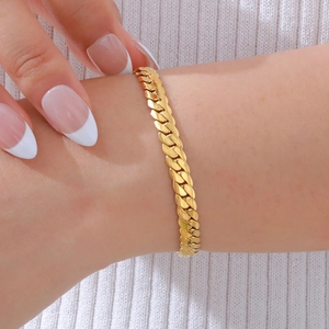 Dettaglio del bracciale a catena cubana dorata al polso su sfondo in maglia bianca