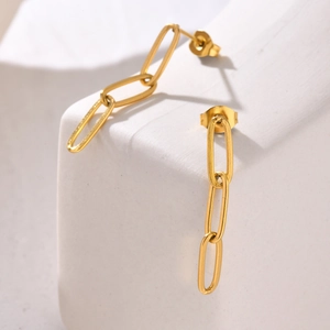 Macro shot of gold stainless steel long oval link earrings on white marble texture