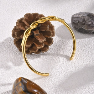 Detail of gold twisted cable cuff bracelet with woven texture on natural stone background
