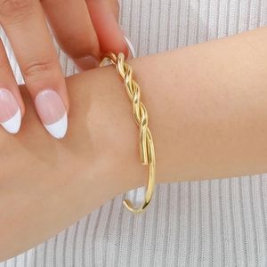 Detailed macro view of a gold-plated twisted cable open cuff bracelet on a female wrist