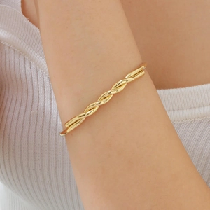Detailed close-up of a twisted gold open cuff bracelet on a woman wrist with knitwear