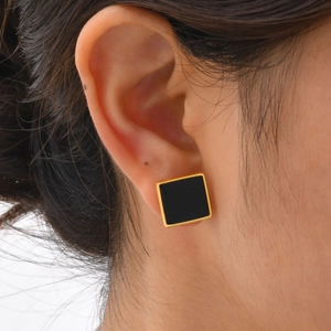 Detailed close-up of a minimalist gold square earring with black enamel worn on the ear