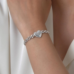 Silver heart pendant bracelet with dotted edge on wrist over white silk background