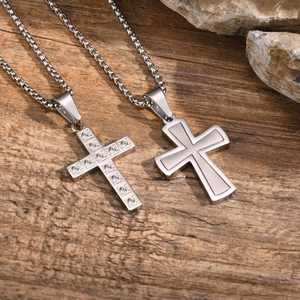 Détail de pendentifs croix argentés avec strass et texture mate sur fond de bois