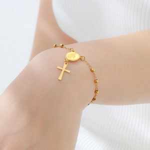 Détail d'un bracelet en acier doré avec perles et breloques Vierge Marie et croix sur un poignet