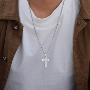 Gros plan d'un collier pendentif croix argenté porté par un homme en tenue décontractée