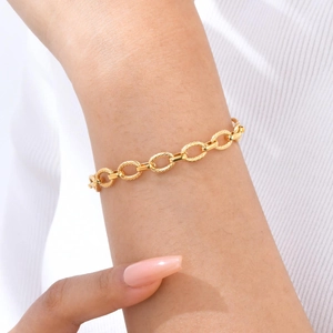 Détail d'un bracelet à maillons dorés gaufrés sur le poignet avec des mailles ovales texturées