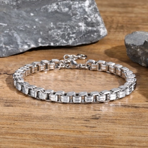 Detailed close-up of a silver stainless steel box chain bracelet on a rustic stone background