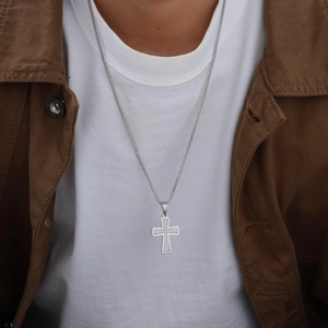 Gros plan d'un collier avec pendentif croix argenté porté par un mannequin homme