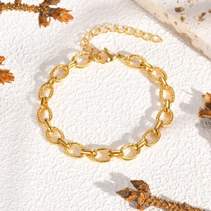 Détail d'un bracelet chaîne doré gaufré avec fermoir mousqueton sur fond de pierre