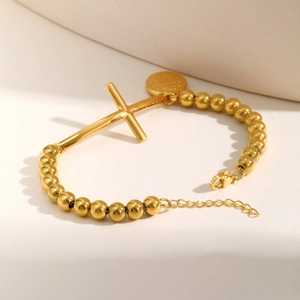 Dettaglio del bracciale a sfere dorate con ciondolo a croce e chiusura a moschettone