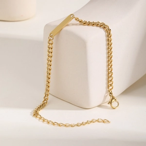 Gros plan d'un bracelet gourmette doré avec plaque rectangulaire et fermoir mousqueton