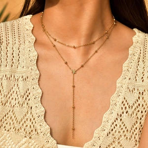 Détail d'un collier en Y doré à double rang avec pendentif marguerite et chaîne perlée